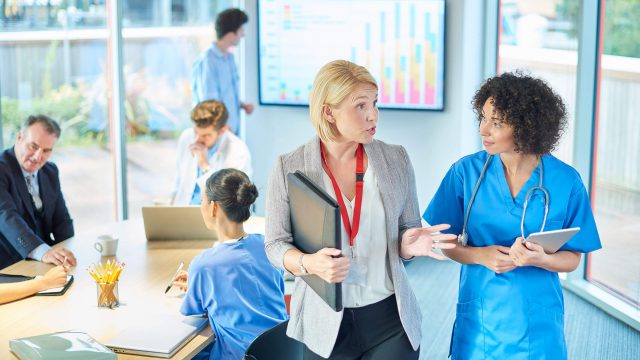 A woman in business clothes meets with nurses in scrubs