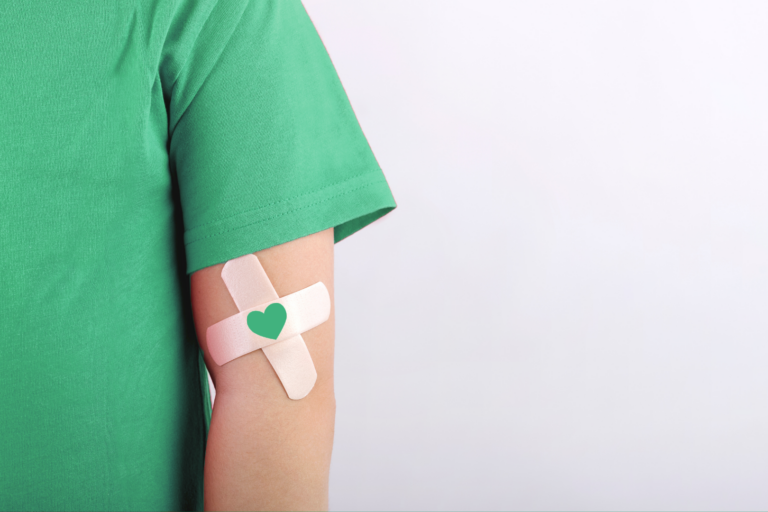 Person wearing green t-shirt sports a cross bandaid with a green heart on their arm