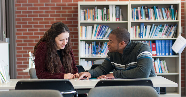 A man points to text in a book as a young woman looks on