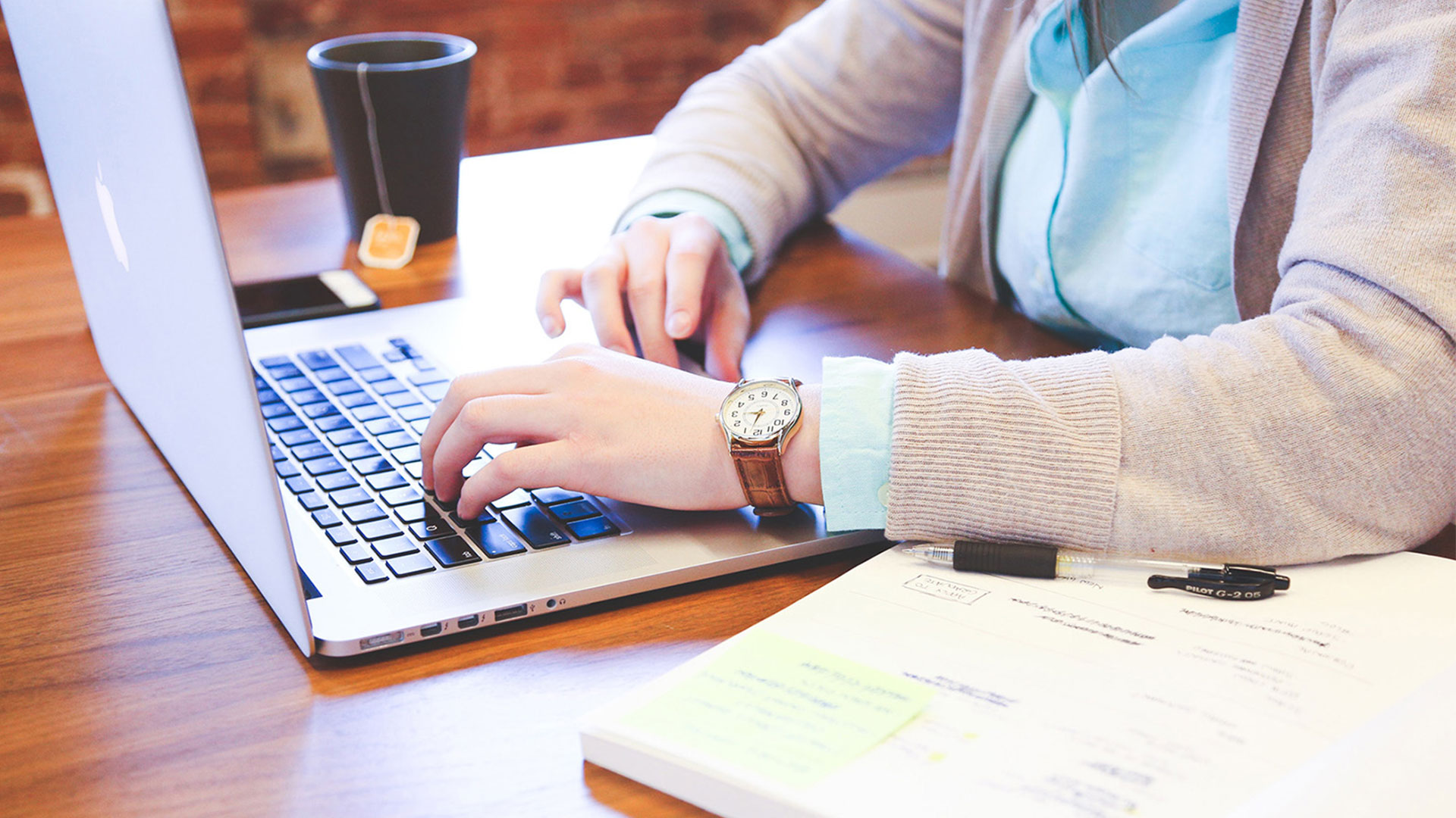 Woman types at laptop. A cup of tea nearby.