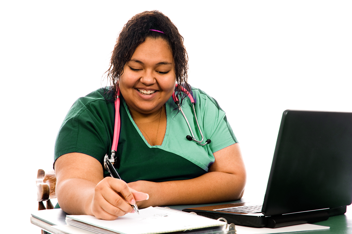 A nurse takes a class online at her desk with a laptop and notebook