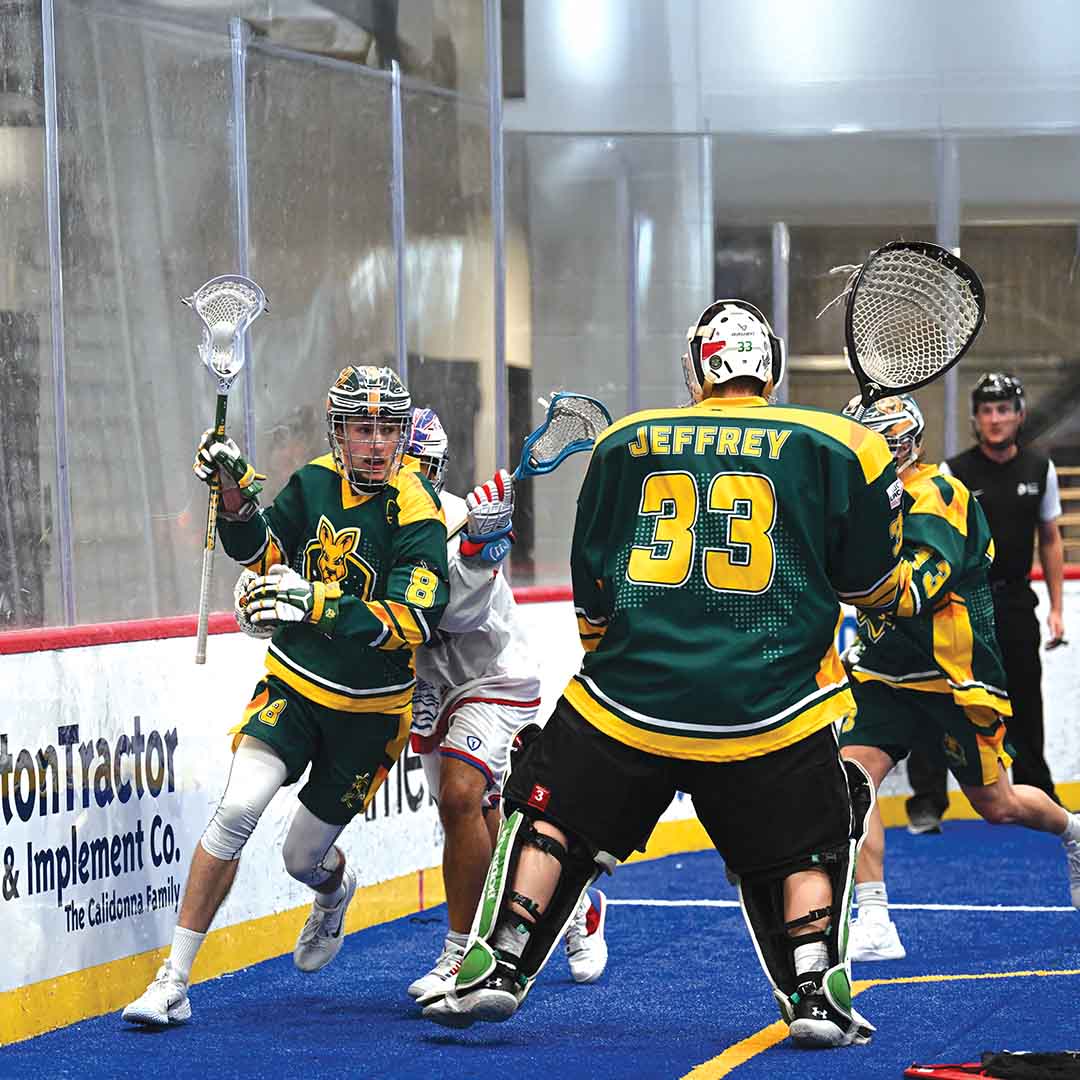 Wildcat lacrosse player facing off with a goalie in an indoor field.