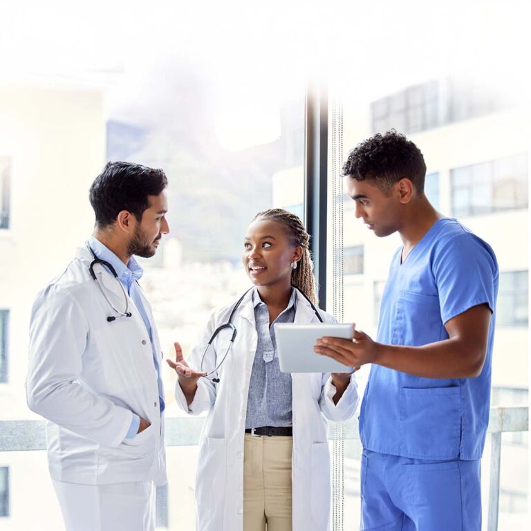 A group of three doctors in a brightly lit hallway smiling and talking.