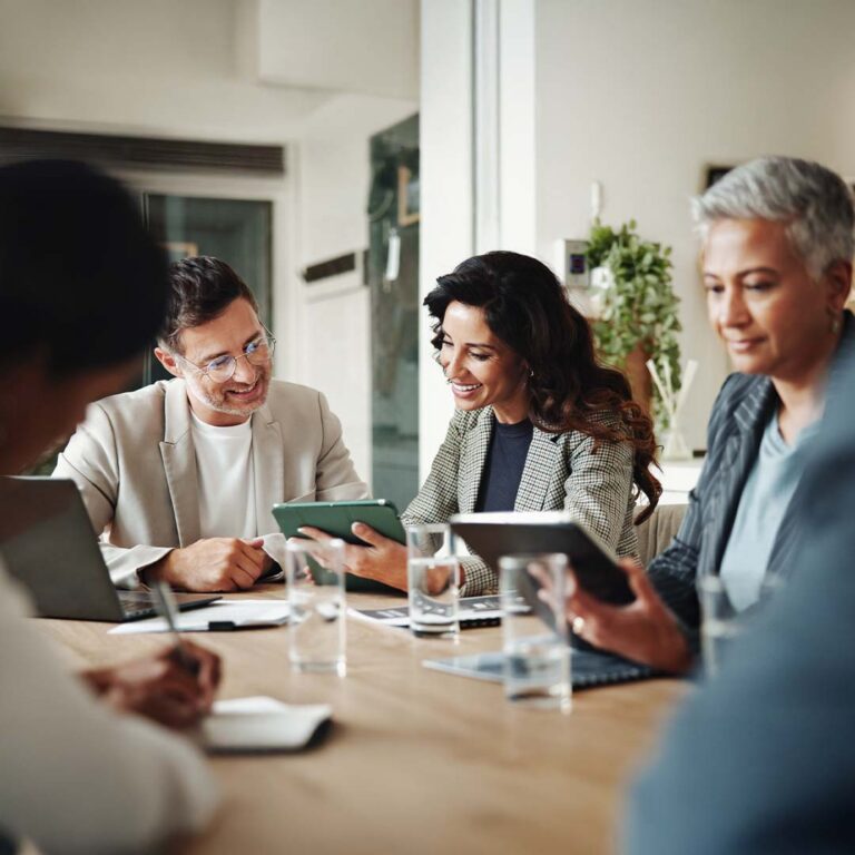 Three business people at a confrence table looking at a tablet.