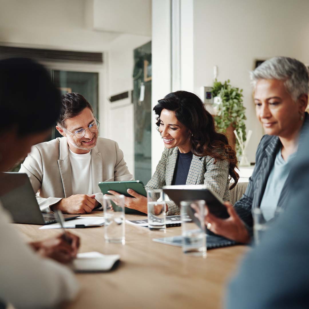 Three business people at a confrence table looking at a tablet.