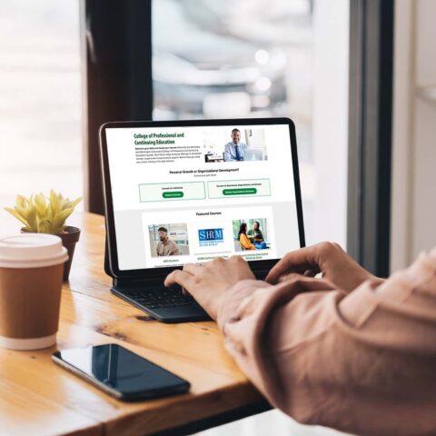 A woman using an ipad in a coffee shop to navigate the new College of Professional and Continuing Education web page.