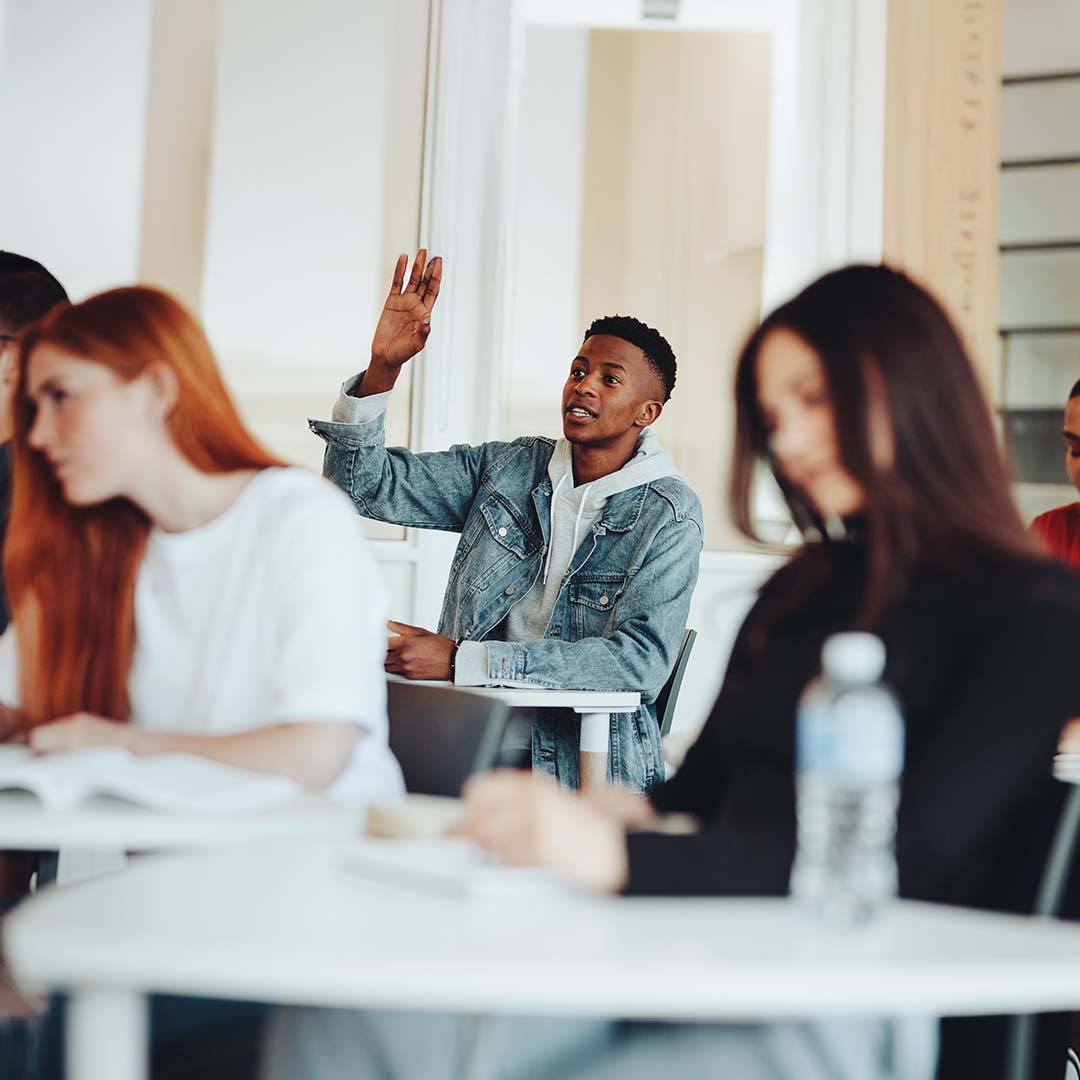 A high school student in a classroom raising their hand.