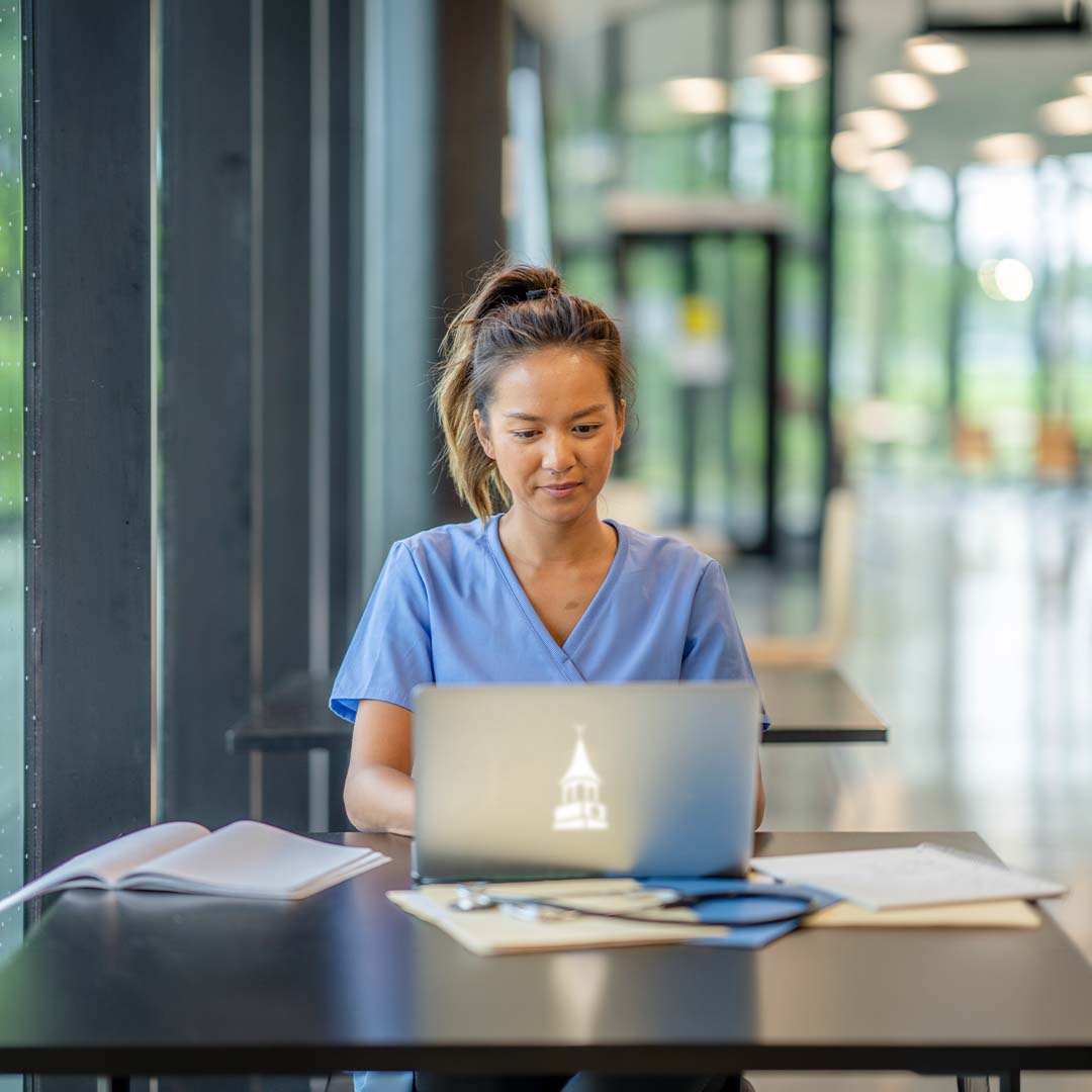 A RN sitting at a table working on a laptop.