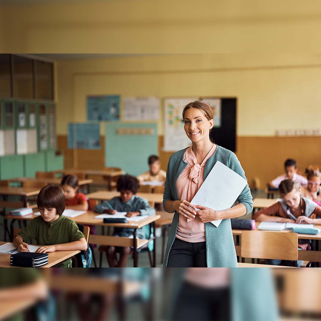 A teacher standing in their classroom with students working at their desks.