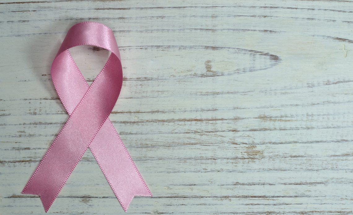 Pink breast cancer awareness ribbon on wooden surface
