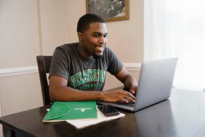Man sits at computer wearing WilmU shirt