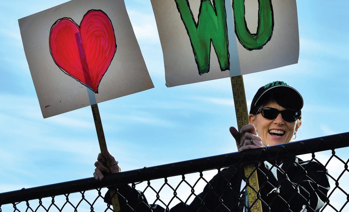 Diane Bansbach hold a heart and WU sign in the stands at a sports game