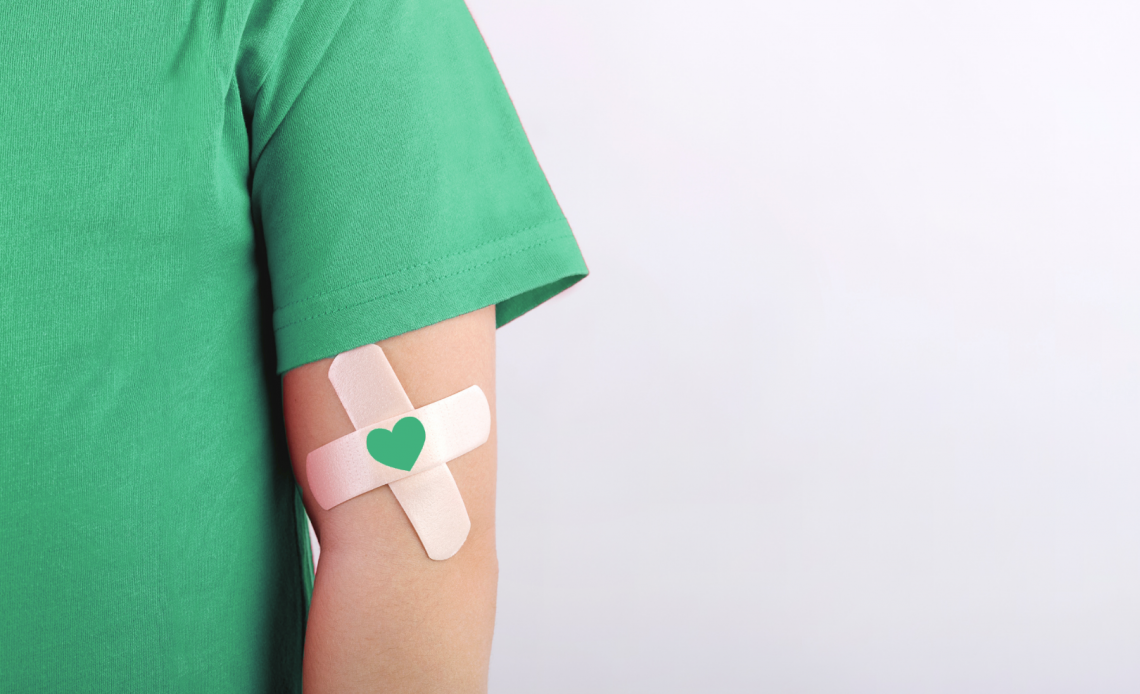 Person wearing green t-shirt sports a cross bandaid with a green heart on their arm