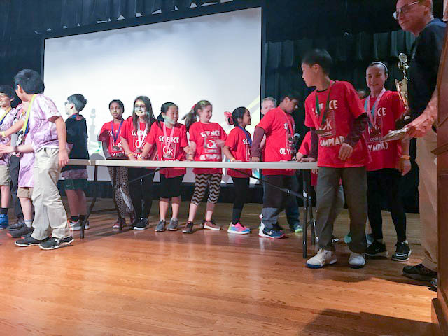 Middle grade children at a table with matching red shirts compete