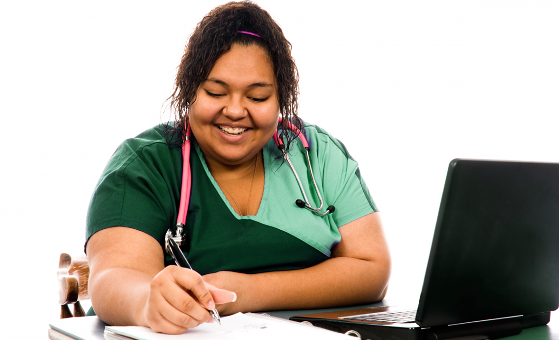 A nurse takes a class online at her desk with a laptop and notebook