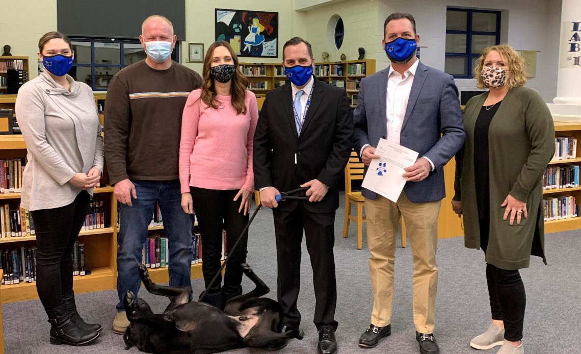 Hammonton Education-Foundation and Princpal Nolan wear masks and stand in a line in front of Wally the dog who lies on his back playfully