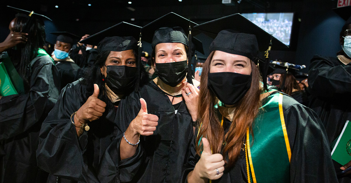 three graduates smiling with thumbs up