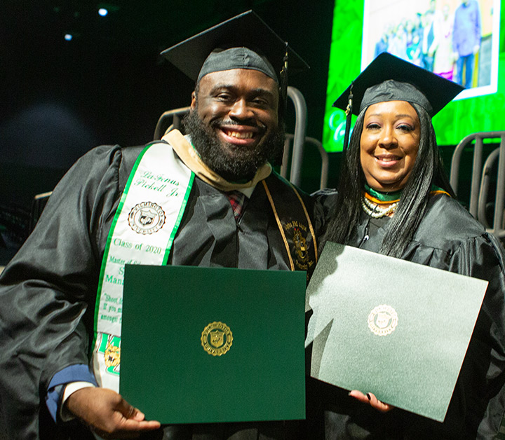 two graduates smiling with diplomas