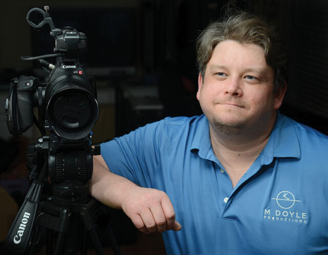 Matthew Doyle leaning on a professional video camera