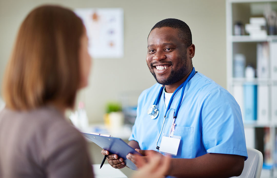 Male nurse talking with a patient and taking notes on a clipboard.