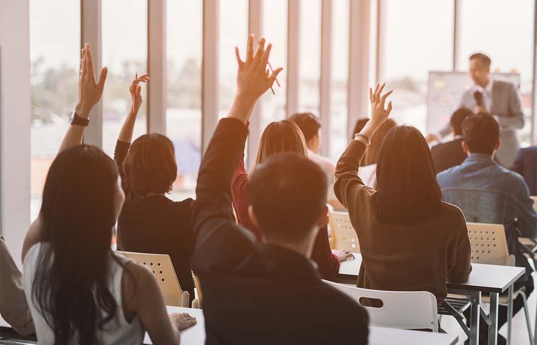 A classroom of business college students raising their hands.